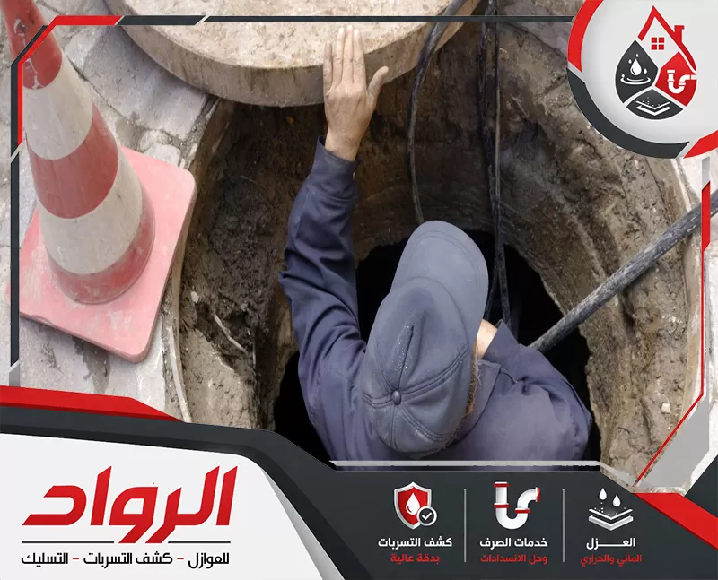 أطلب الأن خدمة تسليك طفح المجاري في الدمام 0562647138 شركة الرواد عاملًا ينزل داخل فتحة صرف أرضية لإجراء أعمال فحص أو تنظيف داخل غرفة التفتيش، مع ظهور غطاء البيارة ومحيط عمل ميداني يشير إلى التعامل مع انسدادات أو مشكلات داخل شبكة الصرف.